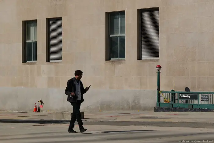 a man walks alone on a sunny street near a subway entrance